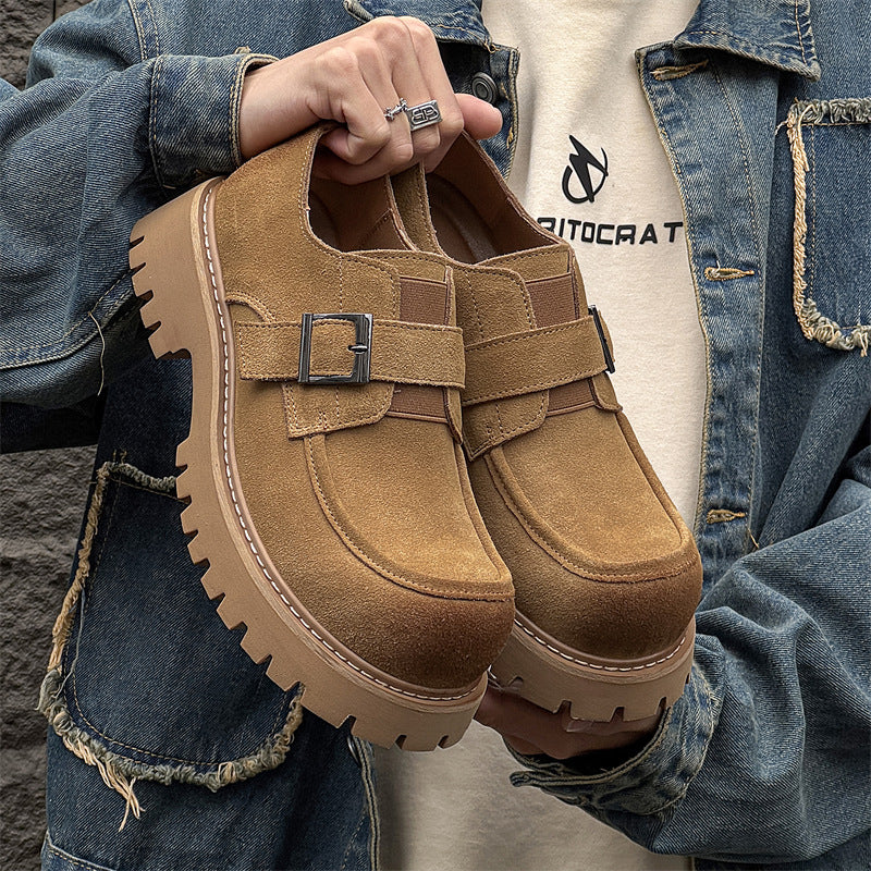 Person holding a pair of brown suede shoes with buckles, wearing a denim jacket and white shirt.